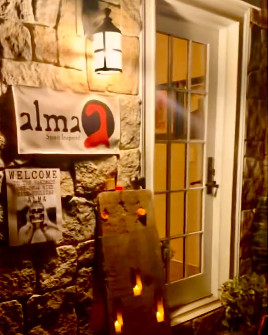 Alma's front door at night: the lantern, the Alma sign, and a candlelit board beside the glass door